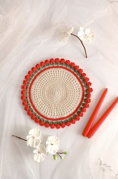 a crocheted doily with flowers and two red handled carrots on a white surface