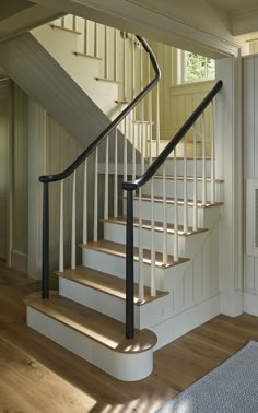 a white staircase with black handrail and wood flooring in a home setting on a sunny day