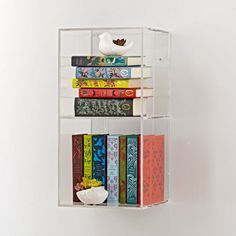 a book shelf with books and a bird on it's top, against a white wall