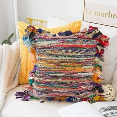 a multicolored pillow sitting on top of a white couch next to a book