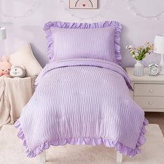 a purple bed in a bedroom next to a white dresser and table with stuffed animals on it