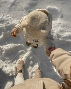 two people standing in the snow holding hands and looking at a teddy bear that is stuck in the snow