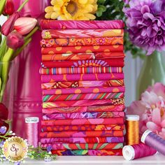 a stack of bright colored fabric next to flowers and spools of thread on a table