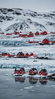 the red houses are surrounded by ice and snow on the water's edge, with mountains in the background