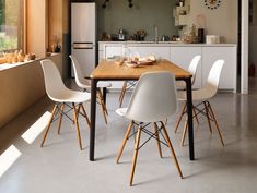 a kitchen table with white chairs next to an open window and refrigerator in the background