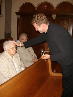 a man standing in front of a wooden bench holding a wine glass with an older woman sitting next to him