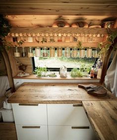 a kitchen area with wooden counter tops and white cupboards under a window filled with potted plants