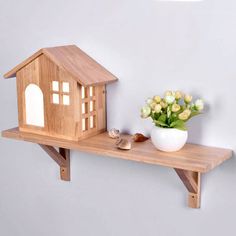 a small wooden house on a shelf next to a potted plant with flowers in it