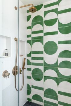 a bathroom with green and white tiles on the wall, shower head, and hand held faucet