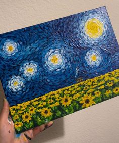 a person holding up a painting with sunflowers in the foreground and a sky full of stars above them