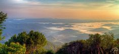 the sun shines brightly through the clouds in the distance, as seen from a mountain top