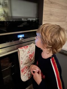 a little boy that is standing in front of an oven and looking at something on the wall