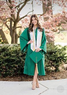 a woman wearing a green graduation gown standing in front of trees