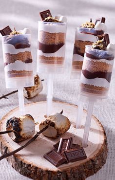 desserts on sticks with chocolate and marshmallow toppings are arranged on a wood slice