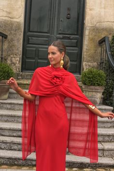 a woman in a long red dress is standing on the steps with her arms outstretched