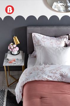 a bed with pink sheets and pillows in a bedroom next to a mirror on the wall