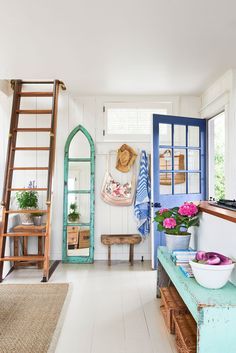 a living room with blue doors and flowers in vases on the table next to a ladder