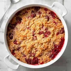 a white dish filled with crumbled fruit on top of a table next to spoons