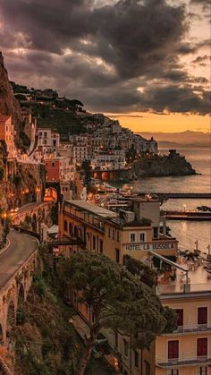 a scenic view of the ocean and buildings at dusk with clouds in the sky above