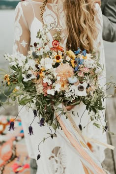 a woman holding a bouquet of flowers in her hands while standing next to the water