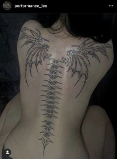 the back of a woman's body with tattoos on her ribs and wings in black ink