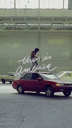 a young man skateboarding on top of a red car in an empty parking lot