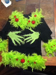 some fake green and red feathers on top of a black t - shirt that is sitting on the floor