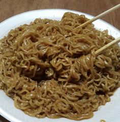 a white plate with noodles and chopsticks in it on top of a wooden table