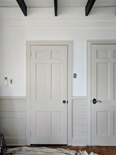 two white doors in a room with wood floors and black beams on the ceiling above them