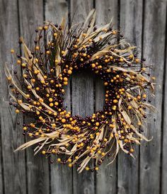 a wreath made out of dried grass and berries on a wooden fence with the word fall written across it