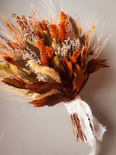 an arrangement of dried flowers and leaves on a white cloth tied to a gray wall