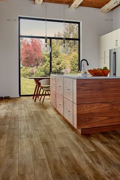 a kitchen with wood flooring and white cabinets in the background, an open window looks out onto a yard