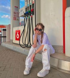 a woman sitting on the curb next to a gas station with her hand under her face