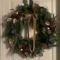 a christmas wreath hanging on a door with gold and silver ornaments around it, along with greenery