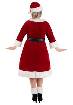 a woman dressed in a santa suit and black boots is standing with her arms outstretched