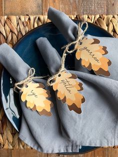 two napkins with tags tied to them sitting on a blue plate next to a woven place mat