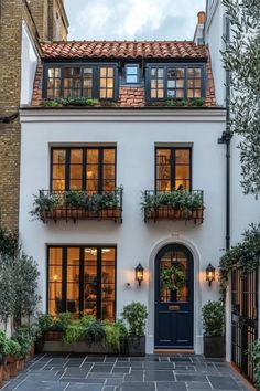 a white house with lots of windows and potted plants on the front door is lit up at night