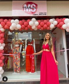 a woman standing in front of a pink and white storefront with balloons around it