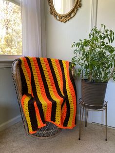 a chair with a blanket on it in front of a potted plant and mirror