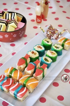 sushi rolls are arranged on a white plate with red polka dot tablecloth and candy in the background