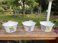 three buckets sitting on top of a wooden table with flowers in the back ground