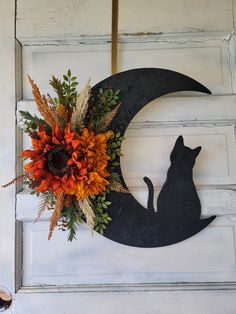 a black cat sitting on top of a moon decorated with flowers and leaves, in front of a white door