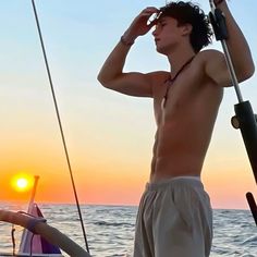 a man standing on top of a boat next to the ocean at sun set with his head in his hands