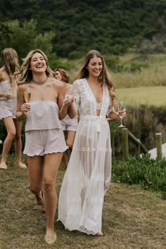 two women in white dresses walking down a hill with one holding a glass of wine