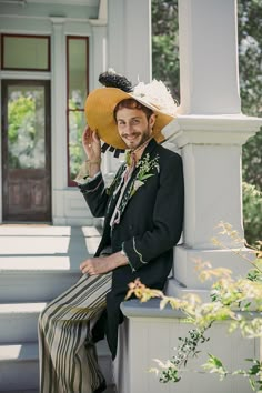 a man wearing a hat and sitting on a porch railing with his hand in his hair