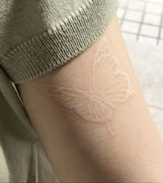 a woman's arm with a white butterfly tattoo on the left side of her arm