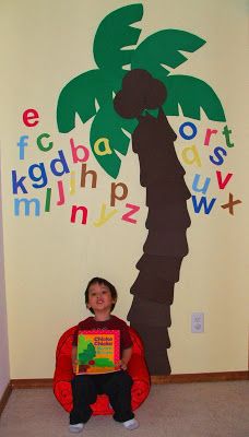 a child sitting on the floor in front of a wall with letters and a palm tree