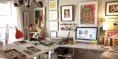 a home office with lots of art on the walls and desks in front of it