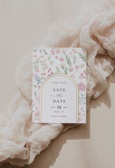 a wedding save the date card on top of a white sheet with pink and green flowers