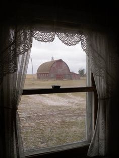 an open window with a view of a barn in the distance and a silo behind it